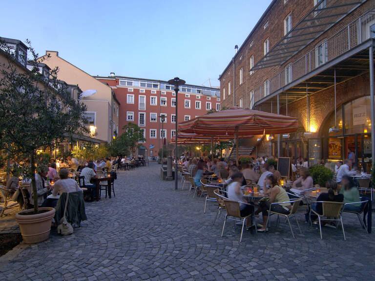 Oberbayerische Altstadt-Gasse bei Dämmerung mit Restaurants und großen Sonnenschirmen