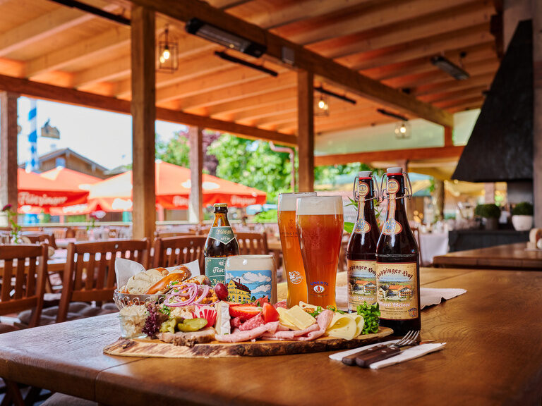 Große Brotzeitplatte auf Tisch in Biergarten, mit Weizengläsern, Brotkorb, Aufstrichen, Käse und Wurst