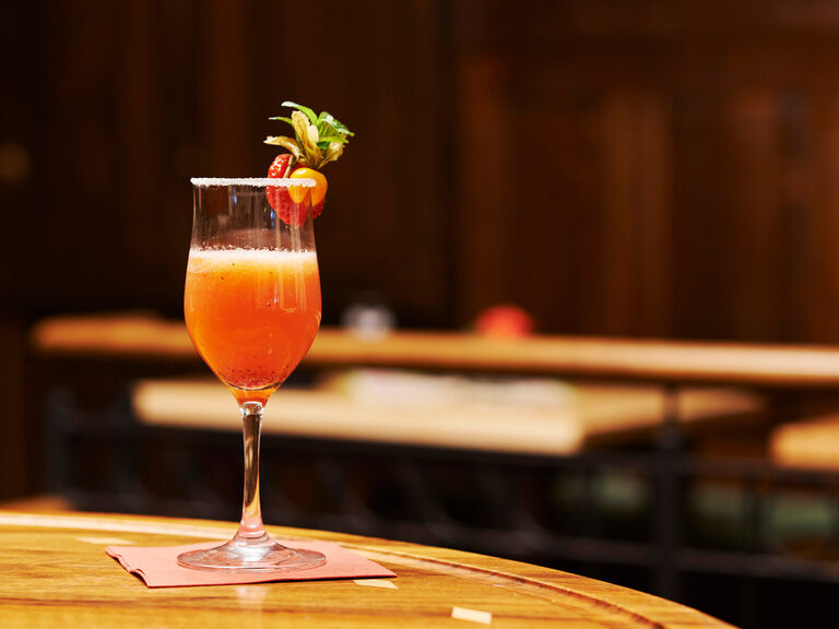 Bunter Cocktail mit Frucht auf Glasrand steht auf Serviette auf Holztisch