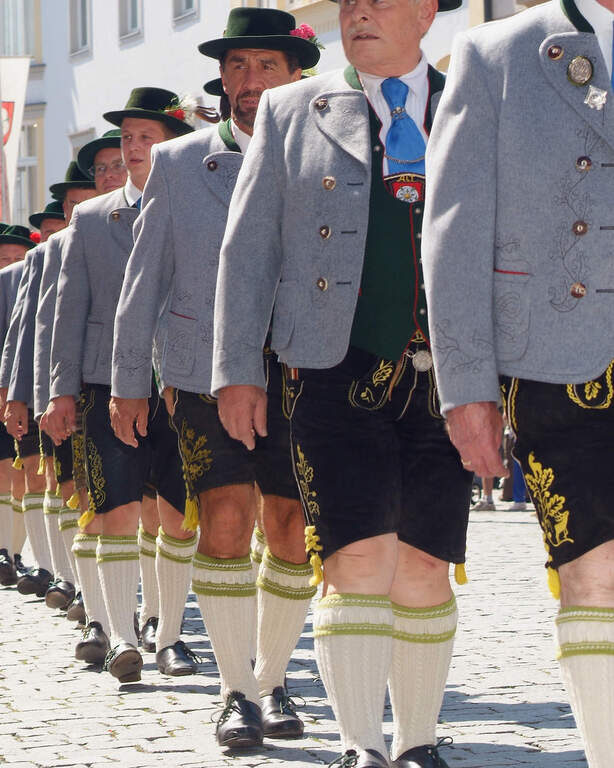 Nahaufnahme mehrerer Männner in Bayerischen Trachten, die bei einem Umzug in einer Reihe schreiten.