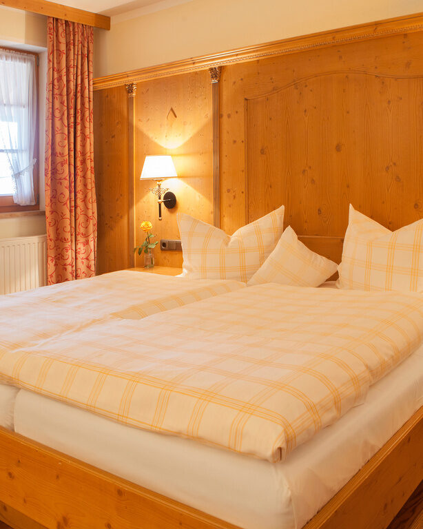 Ein gemütliches Doppelbett in einem Hotelzimmer im Hotel Happinger Hof in Rosenheim mit einladender Beleuchtung