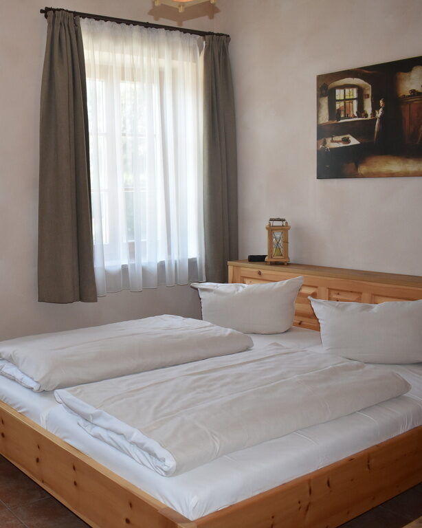 Schlafzimmer von Ferienwohnung mit großem Doppelbett mir Holzrahmen, Holztisch und Stuhl mit Flachbild-TV und zwei Fenstern