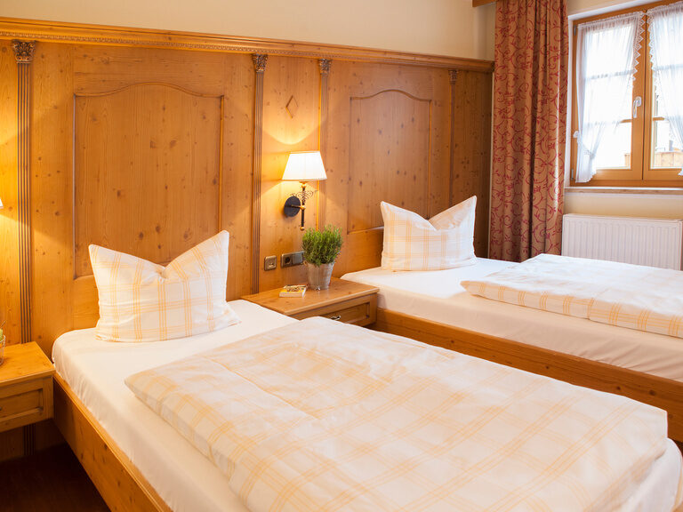 Zwei gemütliche Einzelbetten die nebeneinander in einem Hotelzimmer im Happinger Hof in Bayern stehen.