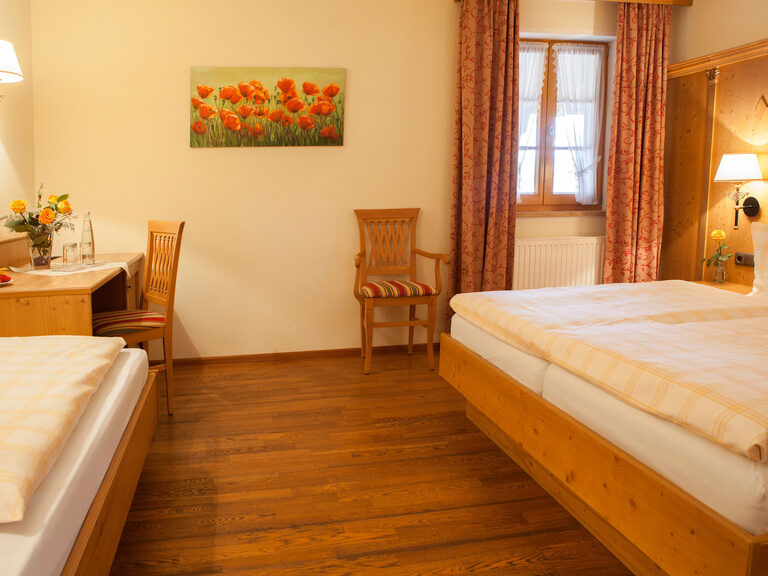 Einblick in ein Schlafzimmer im Hotelzimmer im Happinger Hof mit Holzboden sowie mehreren Betten.