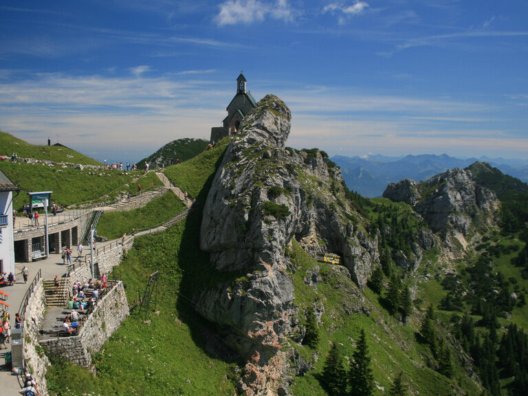 Einkehrmöglich auf einem Berggipfel in den Alpen mit Bergen im Hintergrund und vielen Besuchern