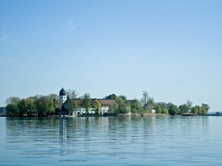 Insel auf einem See mit einer charmanten Kapelle, umgeben von Bäumen und einem tiefblauen Himmel.