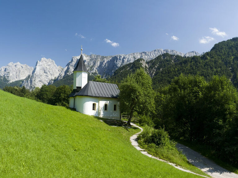 Alpengebirge im Sommer, davor grüne Wiese mit kleiner Kapelle