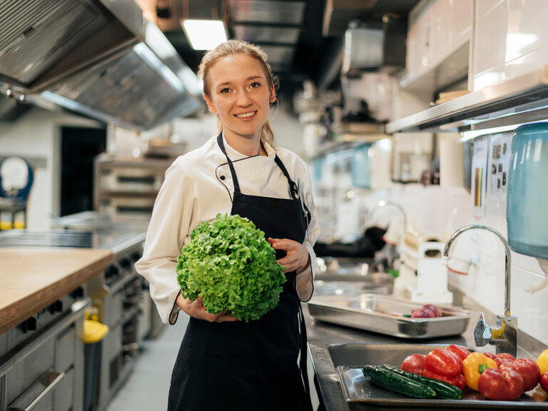 Eine junge Mitarbeiterin der der Küche des Happinger Hof präsentiert einen Salat und frische Zutaten