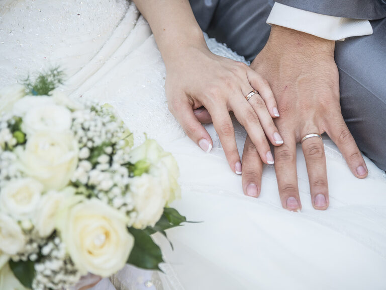Nahaufnahme zwei Hände von Ehepaar mit Blumenstrauß und Eheringe im Hotel Happinger Hof
