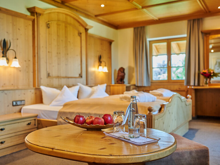 Großes Schlafzimmer in Suite mit Doppelbett mit Holzfassade, Tisch mit Obstschale und Wasserflasche, Blumenstrauß