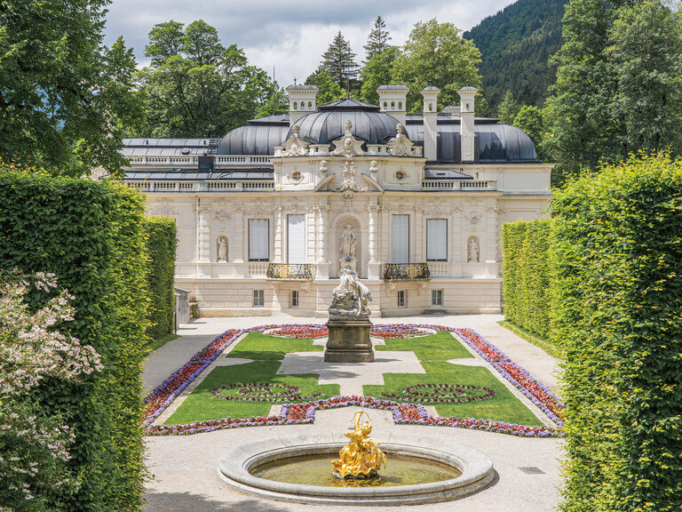 Eindrucksvolles Schloss mit Garten, Statue und goldenem Springbrunnen.