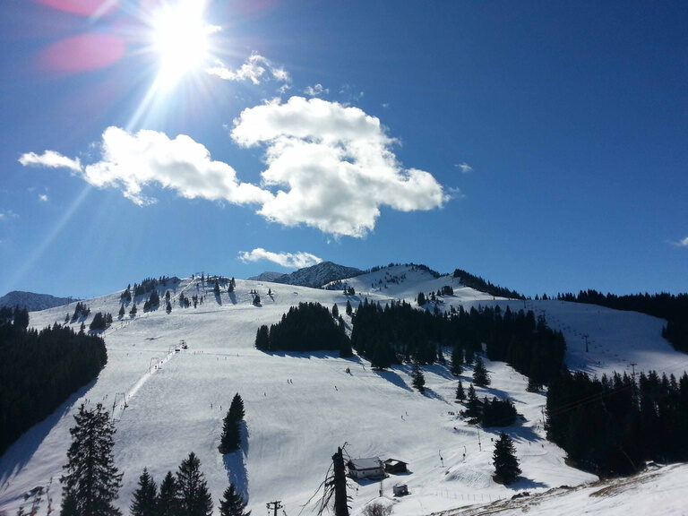 Verschneiter Berg mit Skilift im Winter mit kleinen Wäldern an sonnigem Tag mit Wolken am Himmel