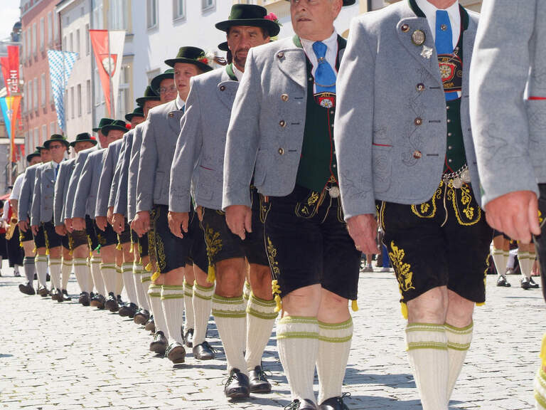 Nahaufnahme mehrerer Männner in Bayerischen Trachten, die bei einem Umzug in einer Reihe schreiten.