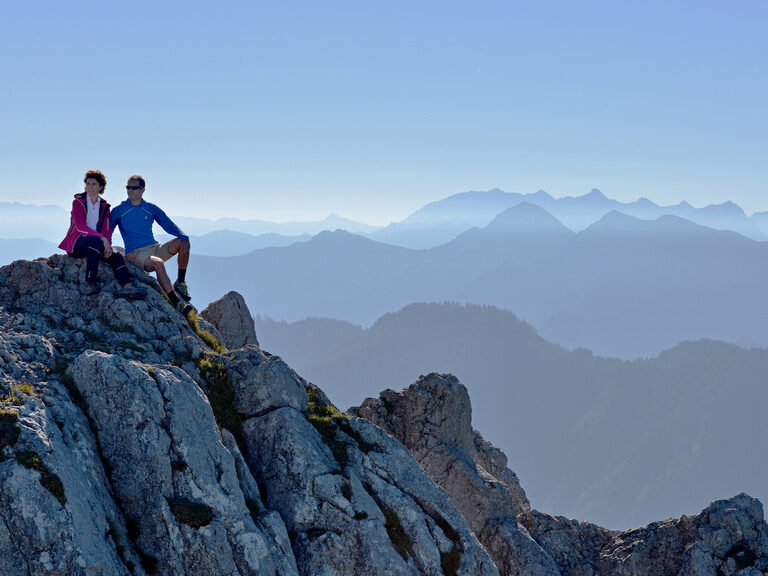 Zwei Wanderer genießen Ausblick auf Steinen auf Gipfel im Alpengebirge