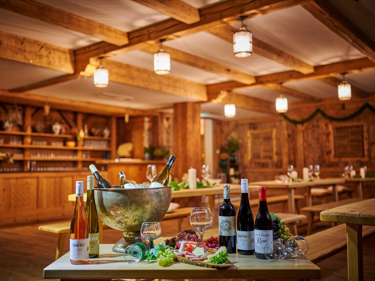 Gedeckter Tisch in traditioneller Weinstube: Weinflaschen, Gläser, Schinken, Käse, Weintrauben, Kühlerbehälter