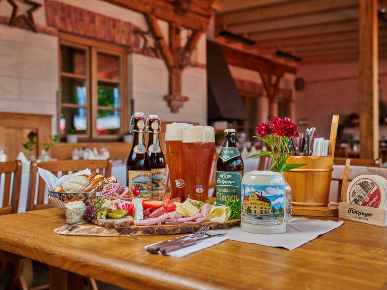 Eine zünftige Brotzeit mit verschiedenem Essen und Bier steht auf einem Tisch in einer Wirtshausstube im Happinger Hof