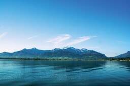 Chiemsee, dahinter grüne Alpenlandschaft und Gebirge im Sommer