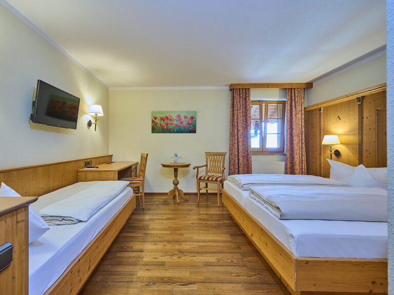 Ansicht eines Hotel-Doppelzimmers im Landhausstil mit vielen Holzmöbeln und TV an der Wand.
