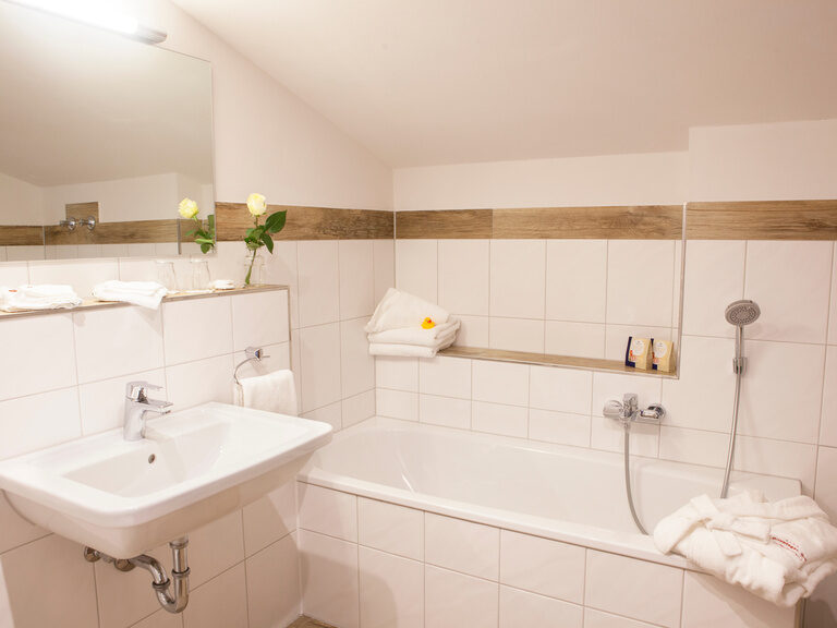 Ein Badezimmer im Hotel Happinger Hof in Rosenheim mit weißer Badewanne sowie Waschbecken.