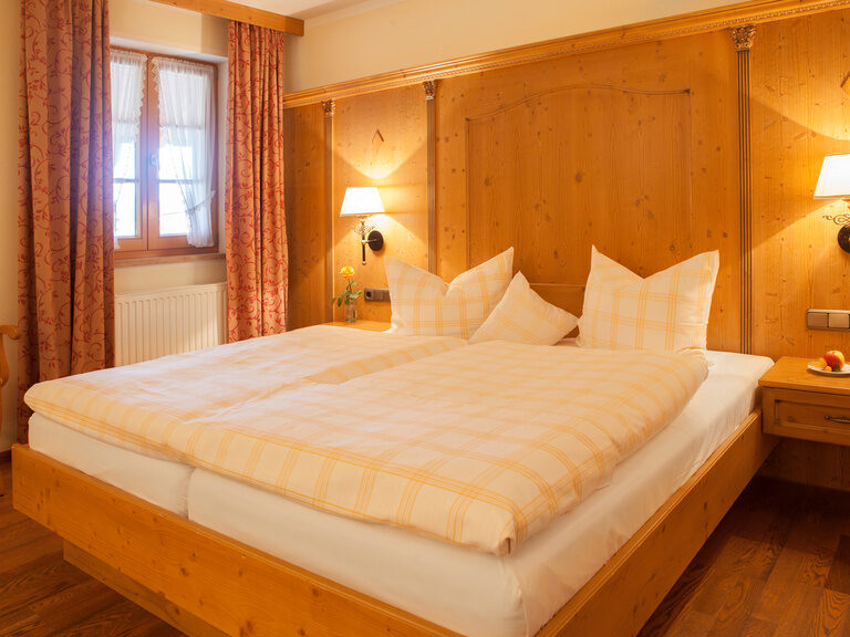 Ein gemütliches Doppelbett in einem Hotelzimmer im Hotel Happinger Hof in Rosenheim mit einladender Beleuchtung