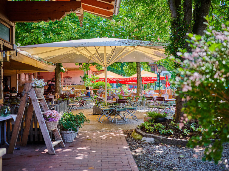 Einblick in Biergarten an sonnigem Tag mit Holzklapp-Stühlen & Tischen