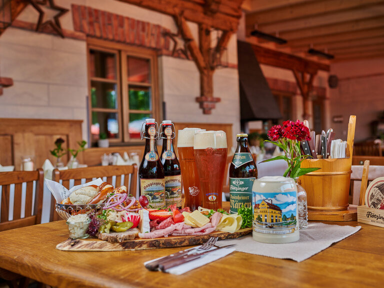 Große Brotzeitplatte auf Tisch in Biergarten, mit Weizengläsern, Brotkorb, Aufstrichen, Käse und Wurst