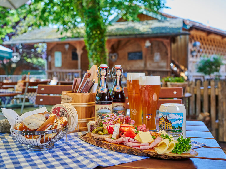 Brotzeitplatte im Biergarten im 3-Sterne-S-Hotel und Landgasthof Happinger Hof in Rosenheim Große Brotzeitplatte auf Tisch in Biergarten, mit Weizengläsern, Brotkorb, Aufstrichen, Käse und Wurst