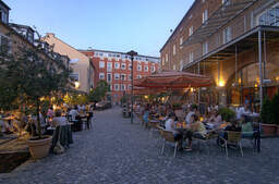 Mehrere Menschen sitzen im Aussenbereich eines Cafes in der Fußgängerzone in der Innenstadt von Rosenheim