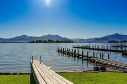 Holzstege führen in sonnenbestrahlten See in Bayern, dahinter Alpegebirge