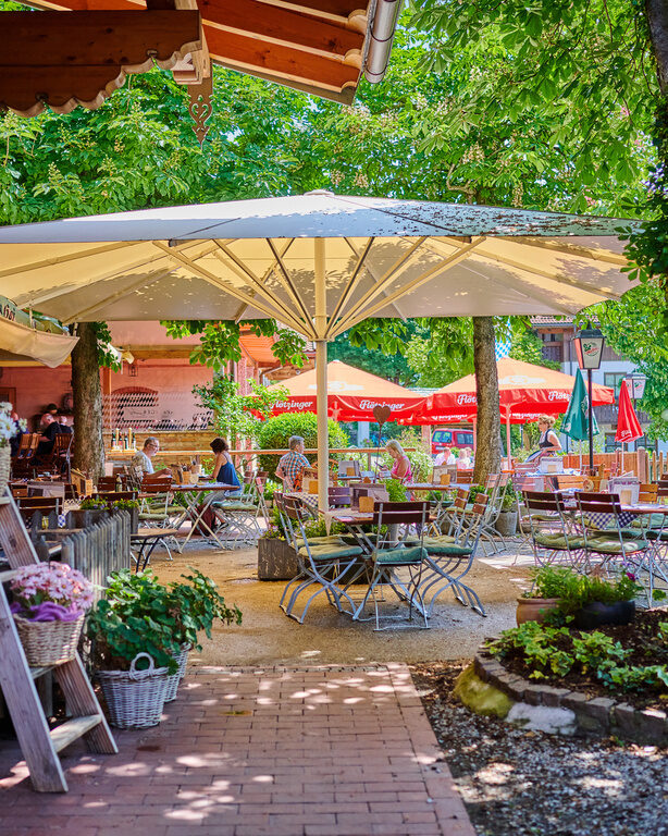 Traditioneller Biergarten mit Holzklappstühlen und -tischen, Sonnenschirmen, Blumen