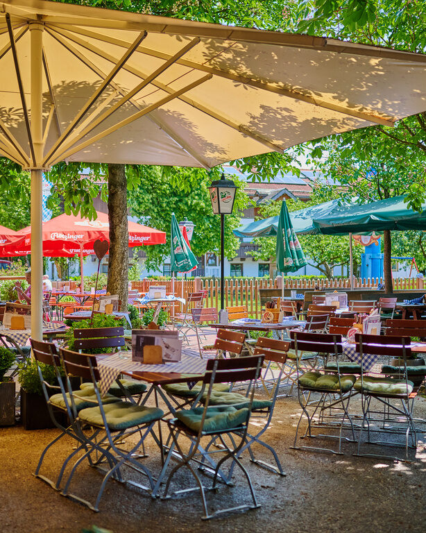 Traditioneller Biergarten mit Holzklappstühlen und -tischen, Sonnenschirmen, Blumen