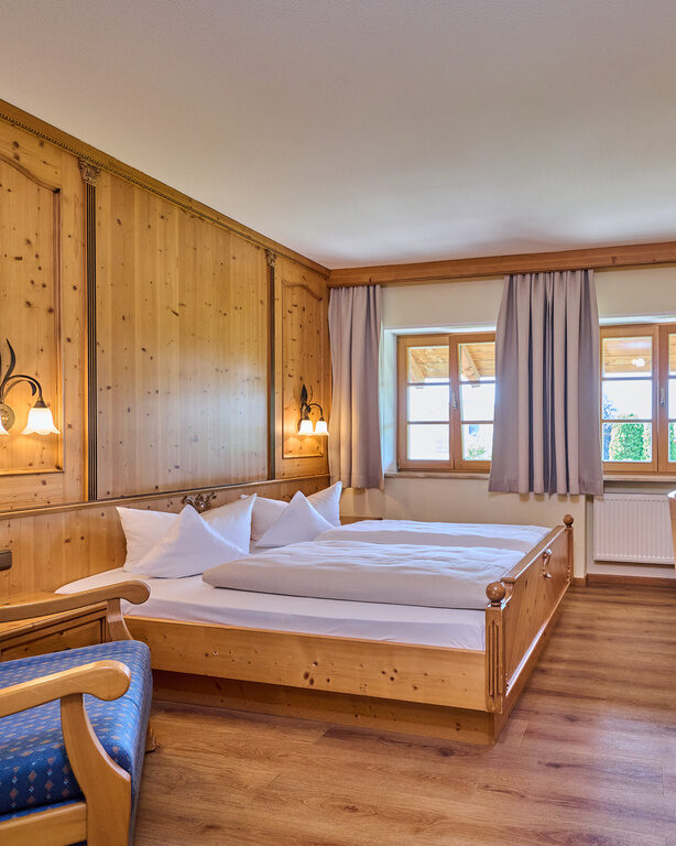 Traditionelles Doppelzimmer mit zwei Fenstern, Holzparkett, Tisch und Stoffsessel