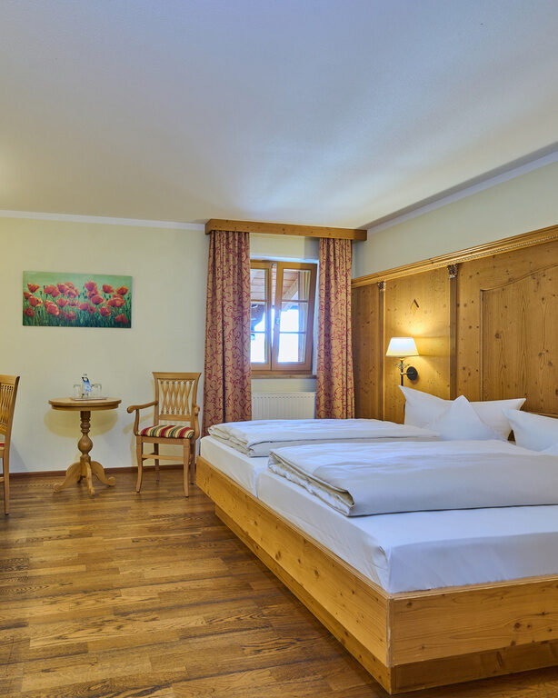 Ansicht eines Hotel-Doppelzimmers im Landhausstil mit vielen Holzmöbeln und TV an der Wand.