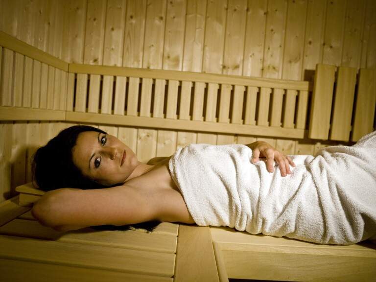 Dame liegt auf dem Rücken in Holz-Sauna, in einem Handtuch gewickelt