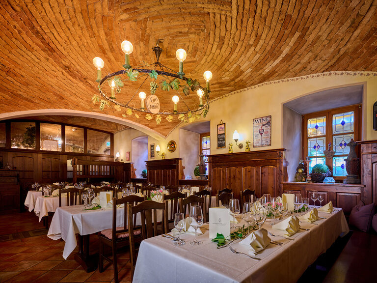 Festlich dekorierte Stube mit weißen Tischdecken, Servietten, antikem Kronleuchter und steinerner Decke