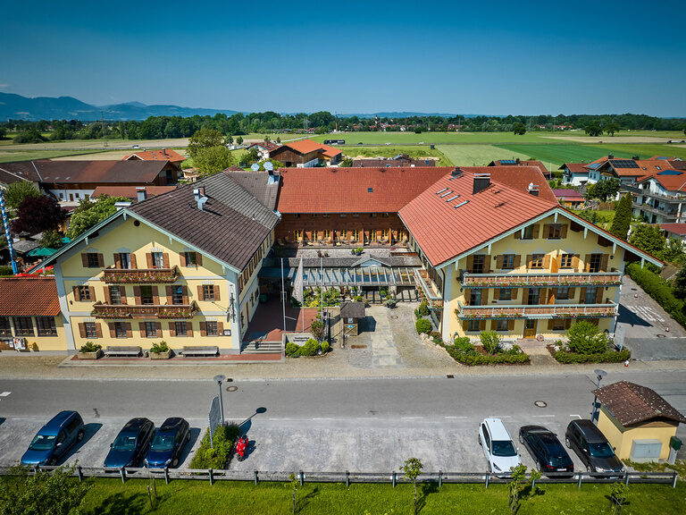 Drohnen-Frontansicht des Dreiseithof Hotel Happinger Hof in Oberbayern Drohnen-Frontansicht des Dreiseithof Hotel Happinger Hof an sonnigem Tag
