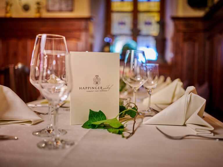 Nahaufnahme von festlich gedeckten Tisch mit Serviettenformen, Weingläsern und Speisekarte mit Logo