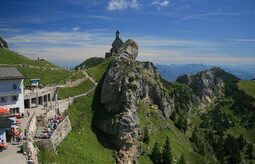 Einkehrmöglich auf einem Berggipfel in den Alpen mit Bergen im Hintergrund und vielen Besuchern