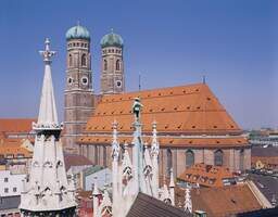Blick auf die Frauenkirche und die Dächer Münchens an einem sonnigen Tag mit blauem Himmel im Hintergrund