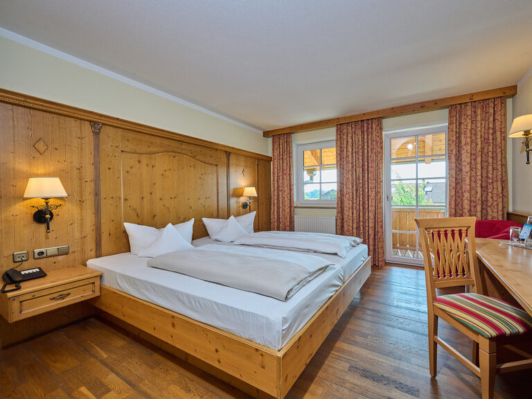 Hotel-Doppelzimmer im 3-Sterne-S-Hotel und Landgasthof Happinger Hof beim Chiemsee Traditionelles Hotel-Doppelzimmer mit Sessel, gemusterten Vorhängen, Balkon und Tisch mit Stuhl