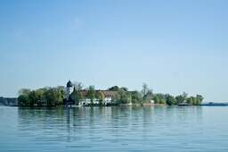 Insel auf einem See mit einer charmanten Kapelle, umgeben von Bäumen und einem tiefblauen Himmel.