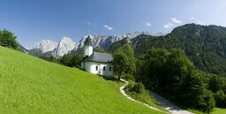 Alpengebirge im Sommer, davor grüne Wiese mit kleiner Kapelle