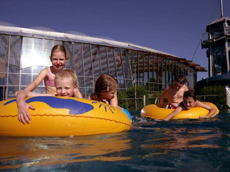 Lachende Kinder auf Wasserreifen in Becken in Außenbereich von Therme