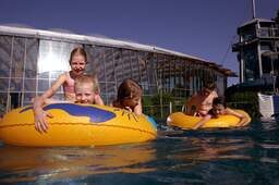 Lachende Kinder auf Wasserreifen in Becken in Außenbereich von Therme