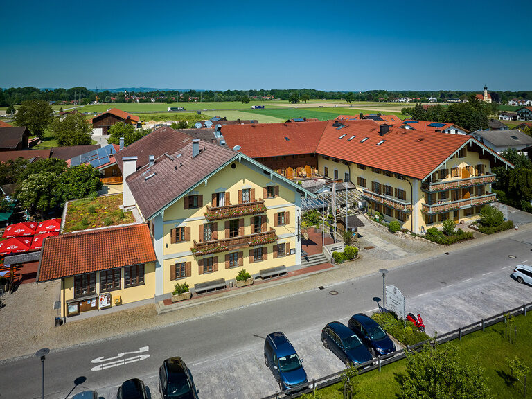 Luftaufnahme Außenansicht vom 3-Sterne-S-Hotel und Landgasthof Happinger Hof beim Chiemsee Luftaufnahme von traditionellem Dreiseithof Hotel und Landgasthof, im Hintergrund Alpen