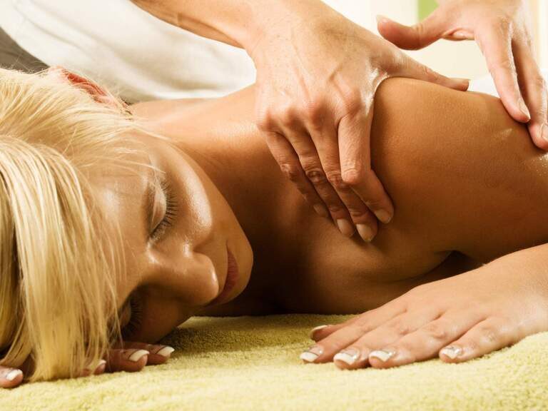 Nahaufnahme Dame bei Rückenmassage im 3-Sterne-S-Hotel und Landgasthof Happinger Hof beim Chiemsee Blonde Dame liegt auf Rücken und genießt eine erholsame Rückenmassage