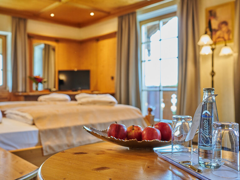 Nahaufnahme Obstschale und Wasser auf Tisch, in Hintergrund modernes Hotelzimmer mit Doppelbett