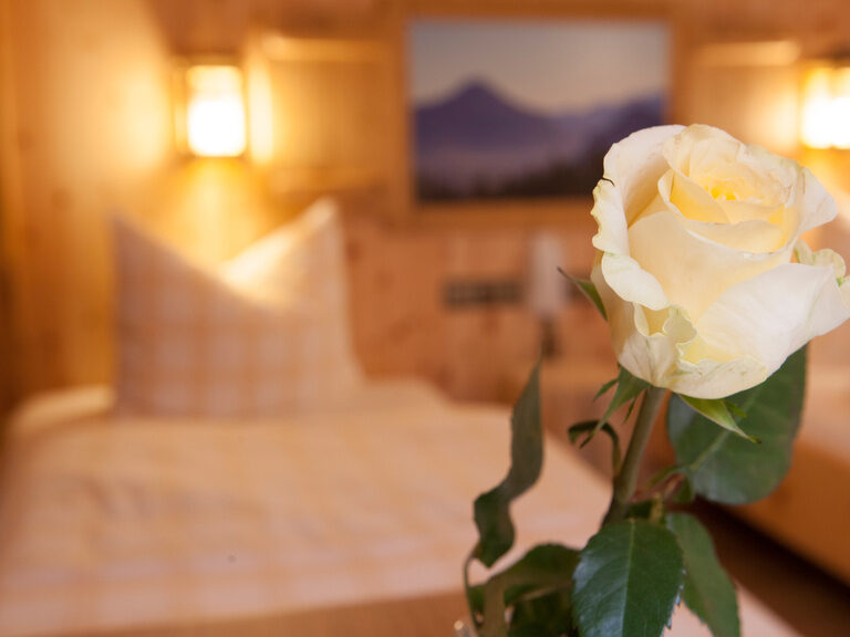 Nahaufnahme einer weißen Rose, im Hintergrund ist unscharf ein Bett des Kranzhorn Twinbettzimmer zu erkennen.
