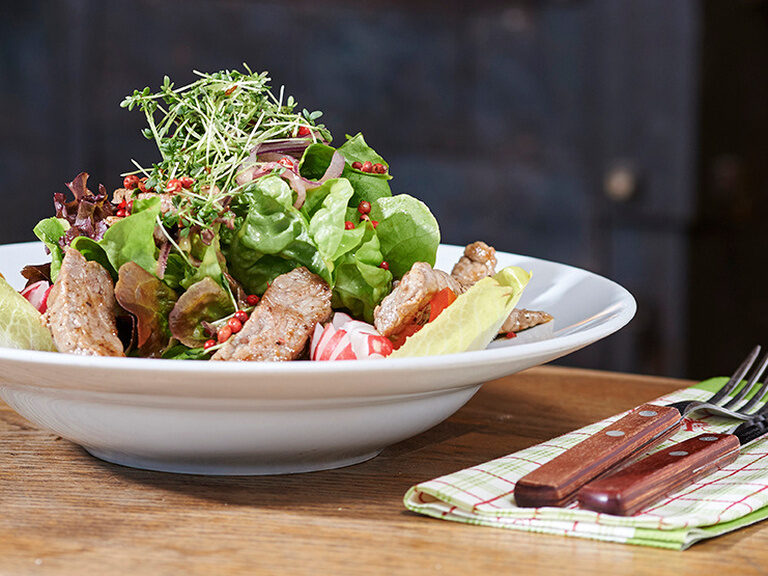 Großer Teller mit buntem Salat und Putenstreifen, daneben Serviette mit Besteck