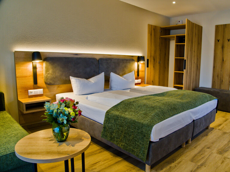 Großes Schlafzimmer in Suite mit Doppelbett mit Holzfassade, Tisch mit Obstschale und Wasserflasche, Blumenstrauß